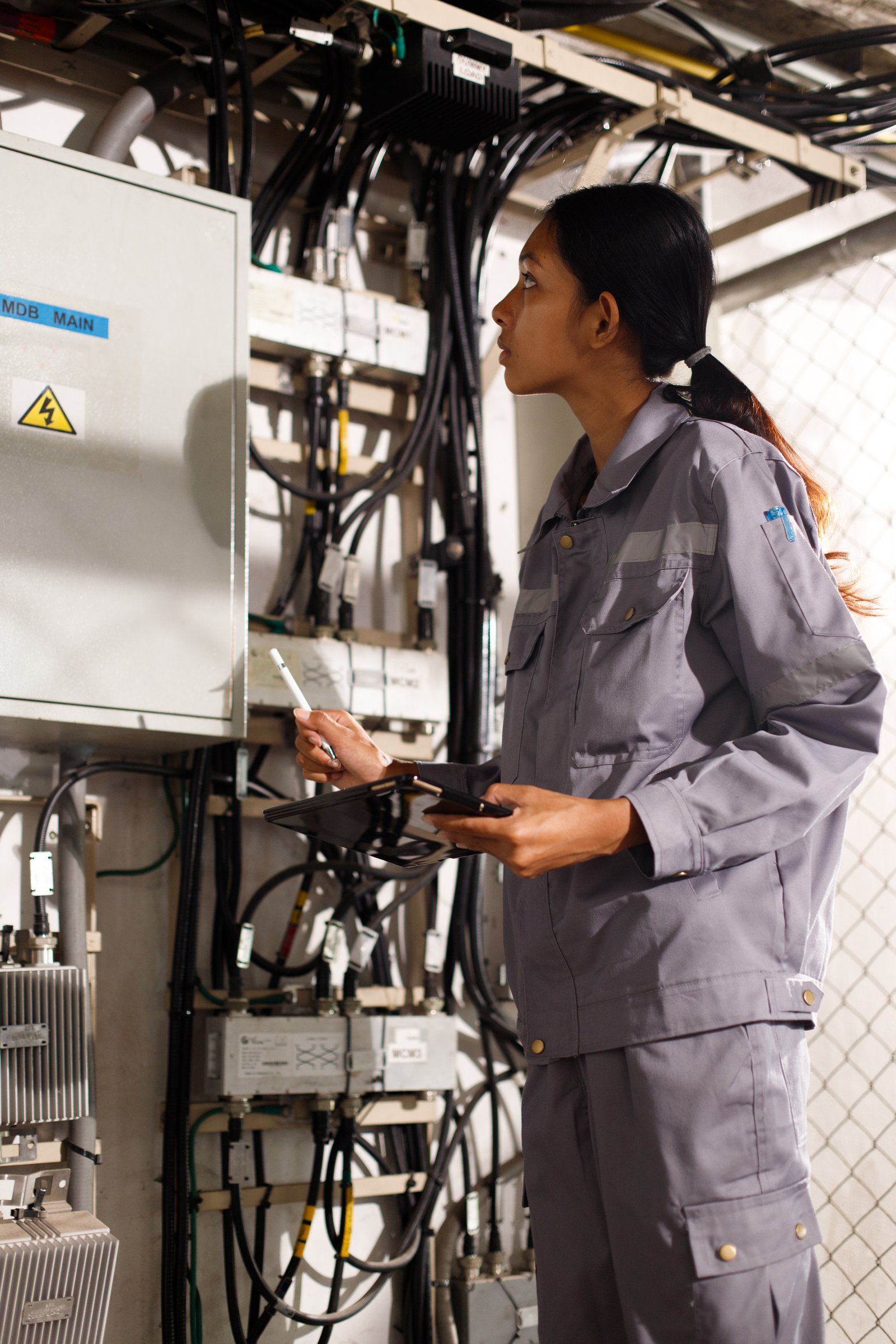 Asian 20s woman in grey uniform as electric fix repair guy. Engineer check inspect wifi signal communication control box power line in Distribution antenna room